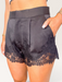 Tucker Brown black satin shorts featuring floral eyelash lace trim, front pleats, and a tailored waist.
