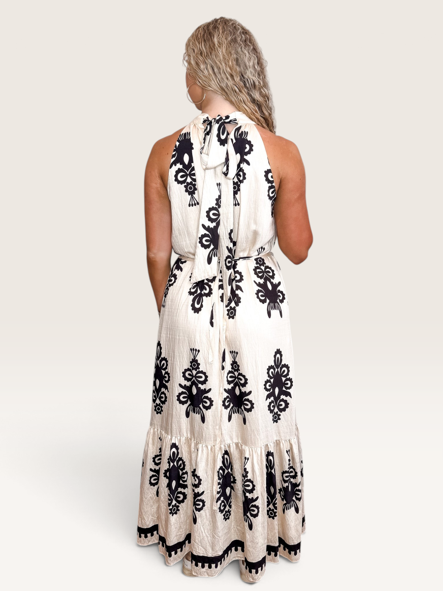 Tucker Brown Liza maxi dress in cream with black floral print, featuring a halter neckline and tie-back detail.