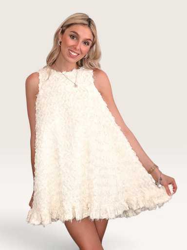 Tucker Brown white babydoll mini dress with eyelash ruffles, mock neck, and pearl buttons worn by a smiling model.