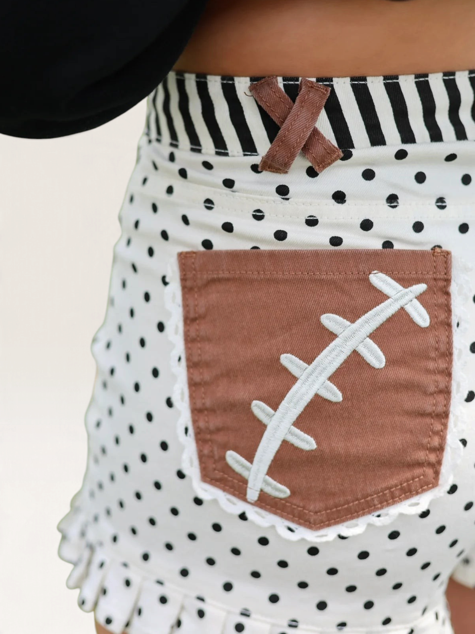 Tucker Brown high-waisted white polka dot shorts with brown football lace pockets and striped waistband detail